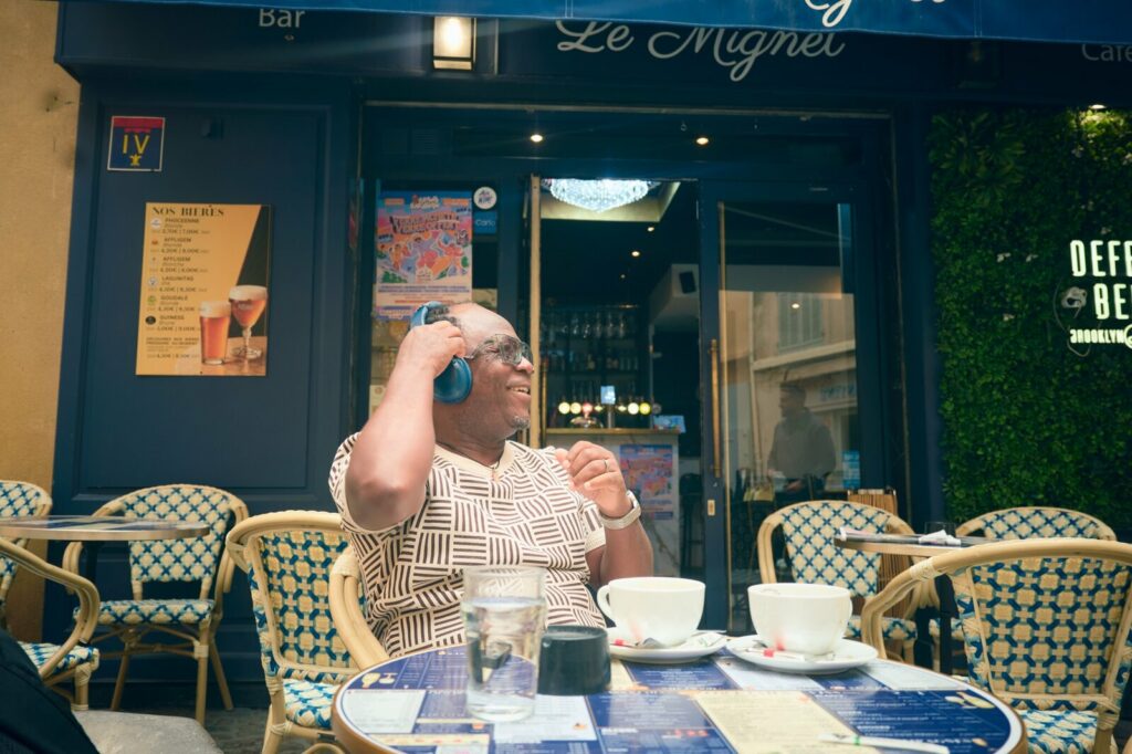 Tchalé rit, un casque sur les oreilles, à une terrasse de café